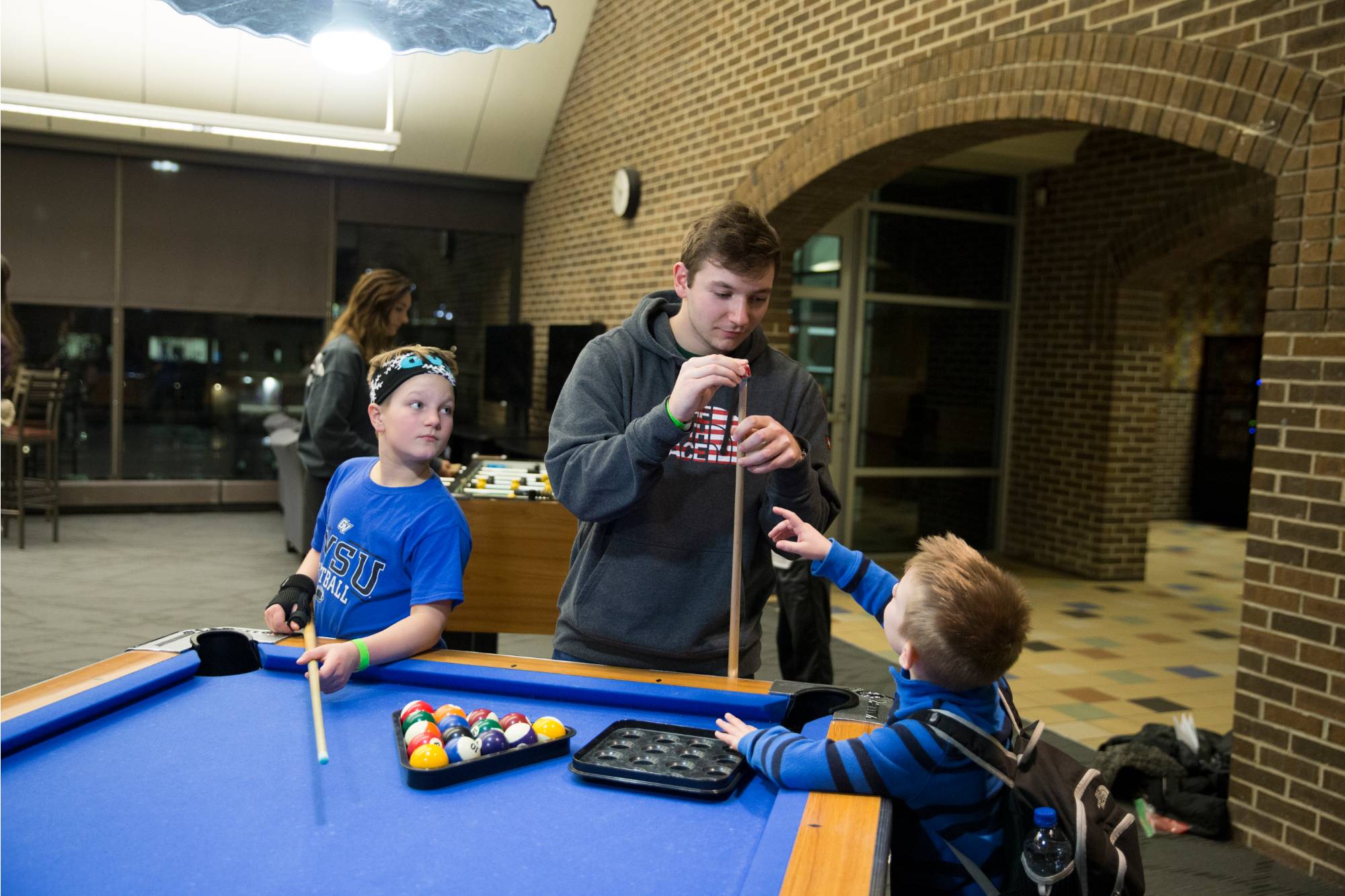 Young siblings and their older brother preparing for a game of pool at the Kirkhof Center